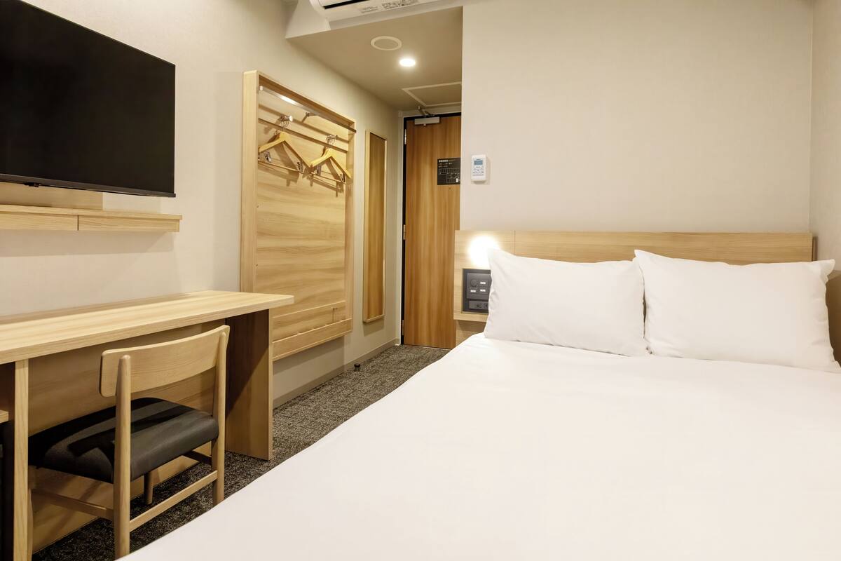 A hotel room with a bed, a desk, a chair, a TV, and a wardrobe.