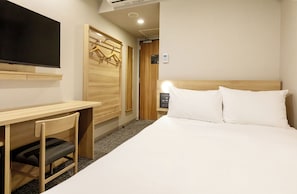 A hotel room with a bed, a desk, a chair, a TV, and a wardrobe.