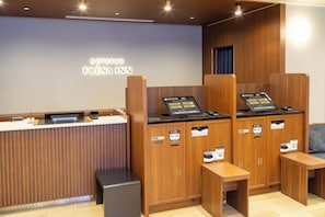 Un espace d’accueil d’hôtel comprenant un comptoir de réception en bois, un écran numérique et un coin salon.