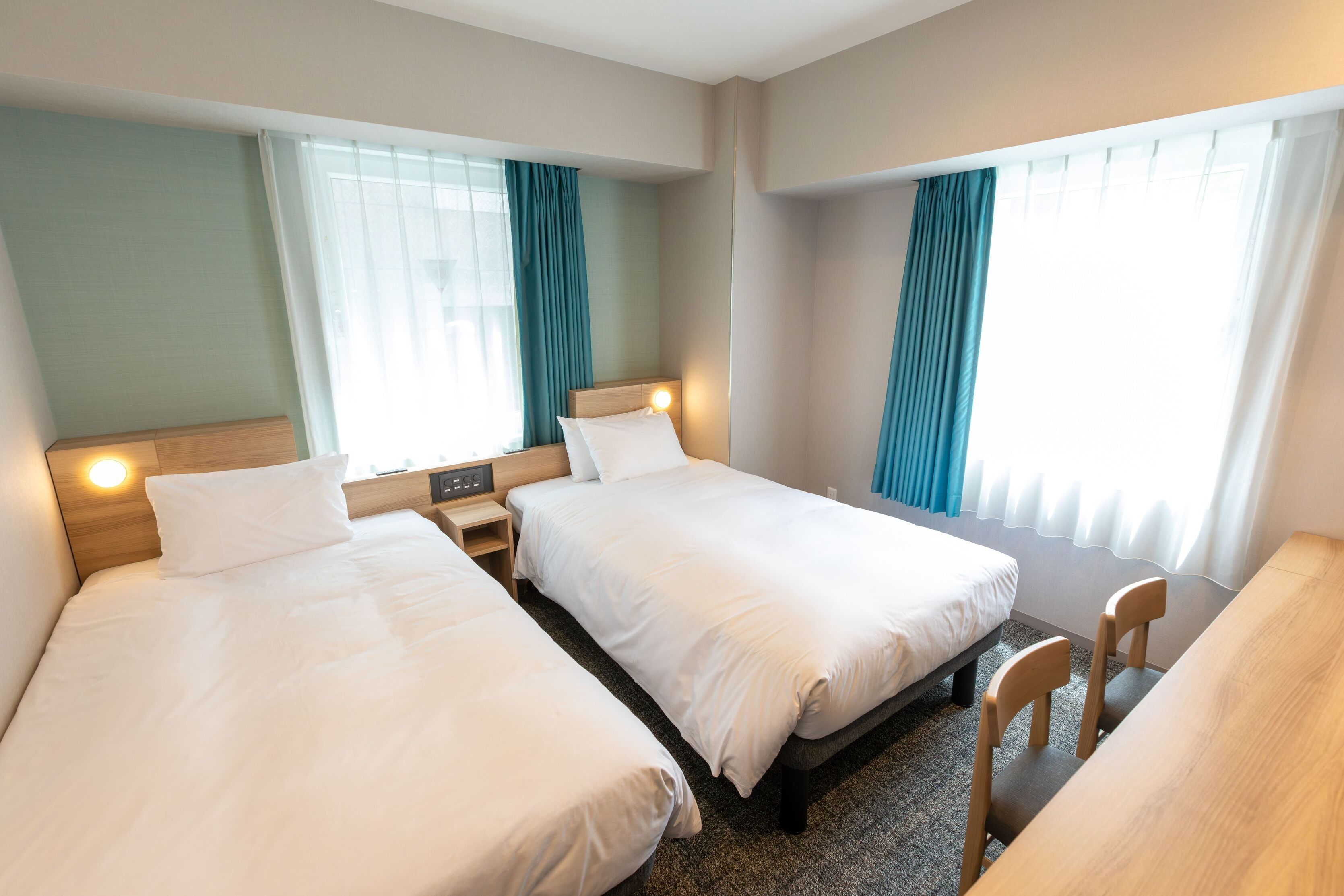 Een hotelkamer met twee eenpersoonsbedden, een houten bureau en een stoel.