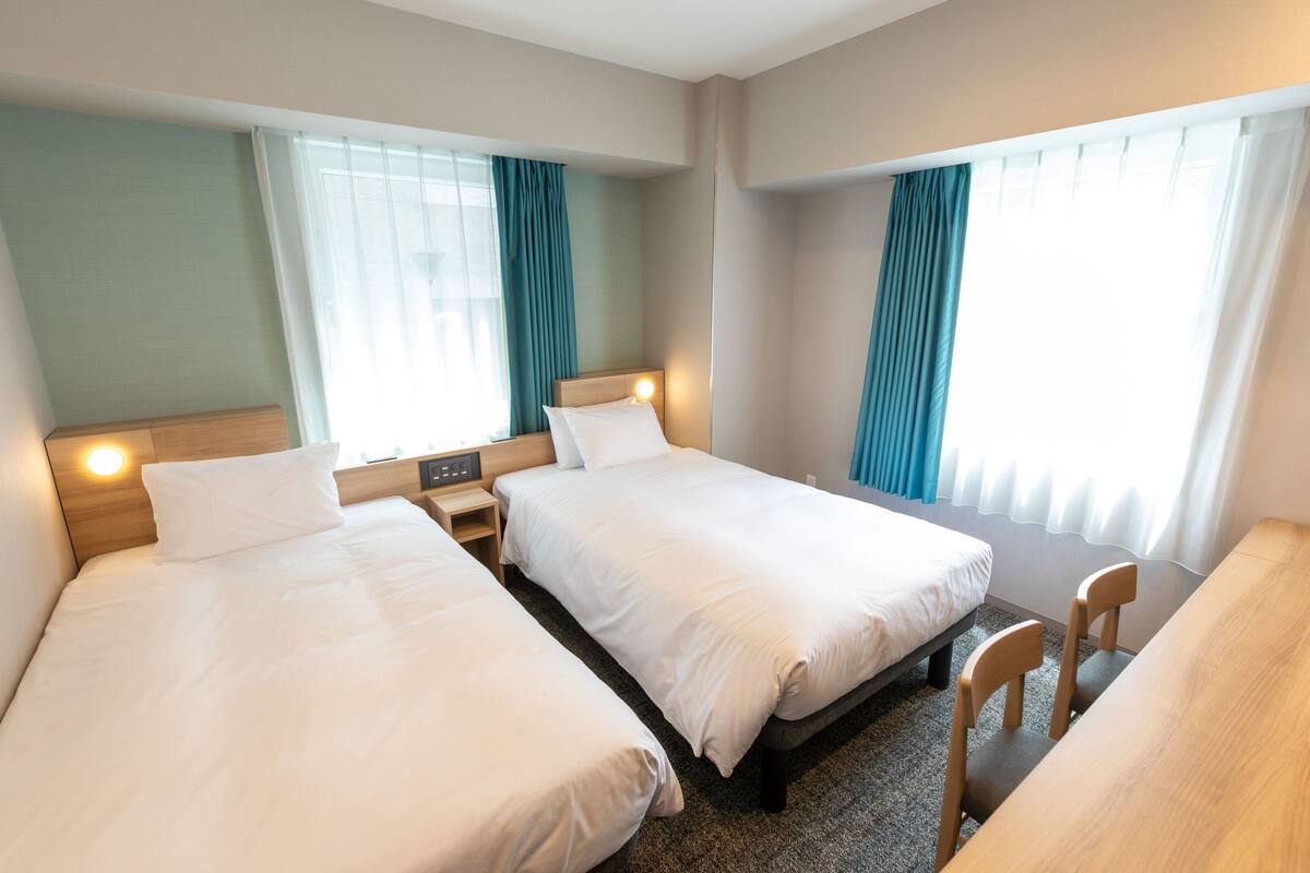 A hotel room with two single beds, a wooden desk, and a chair.