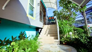 Escadaria que leva a uma casa com fachada azul e branca, cercada por vegetação exuberante e uma área externa coberta.