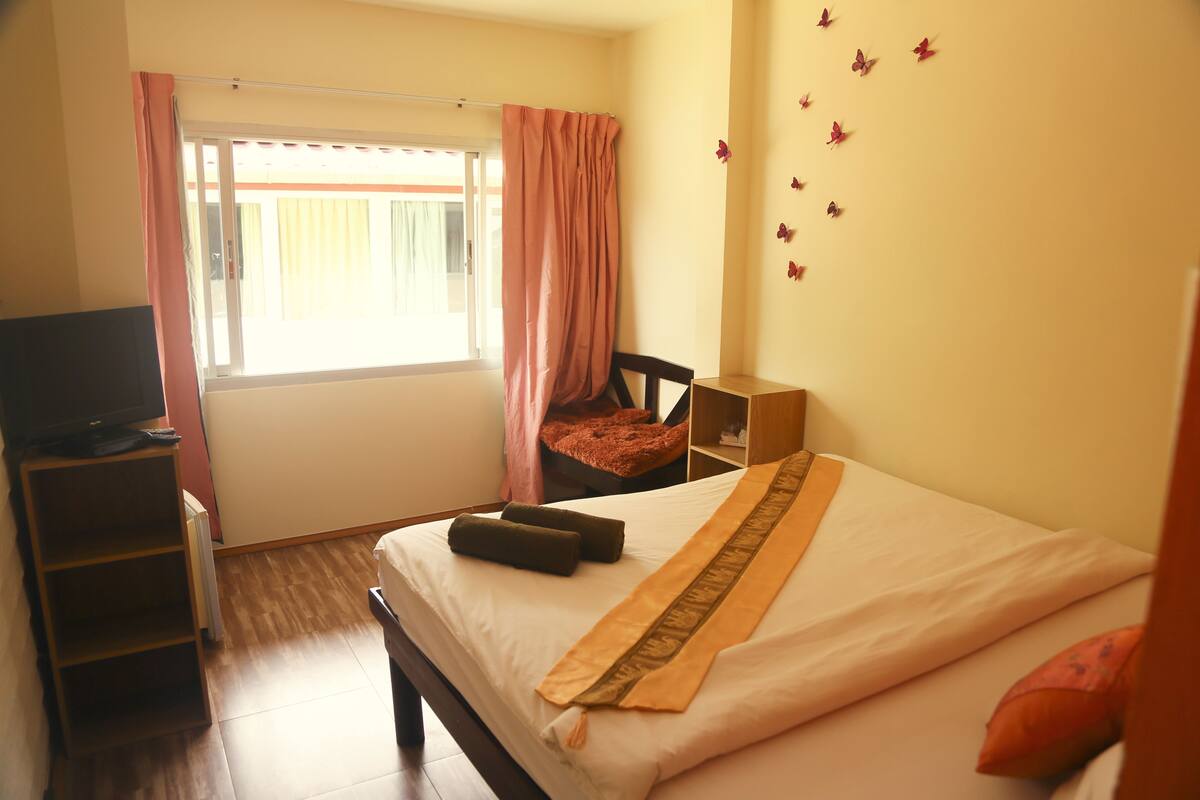 Habitación de hotel con cama, televisión, ventana con cortinas, piso de madera y pared decorada con mariposas.
