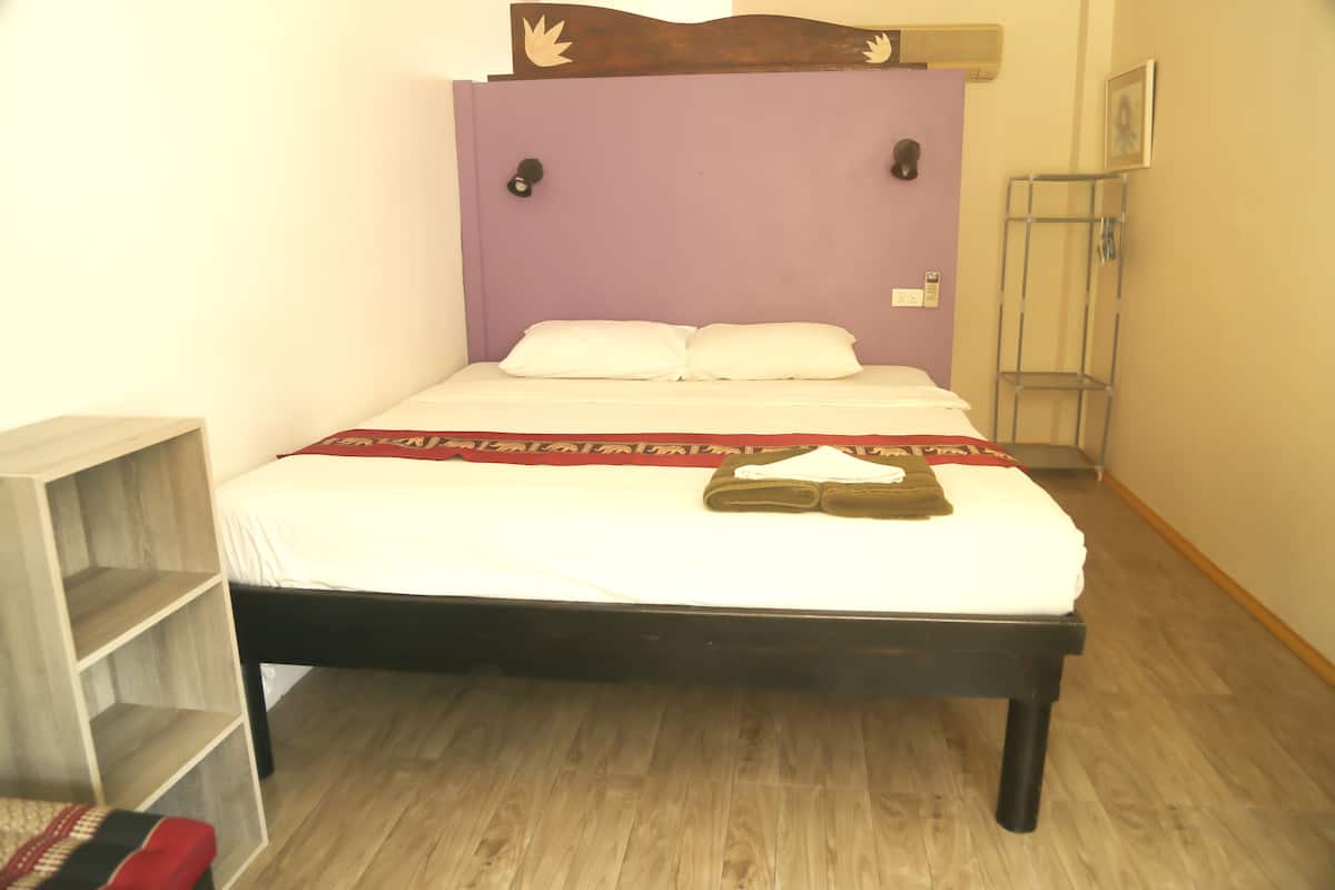 Una cama individual con cabecera de madera, ropa de cama blanca y una colcha roja y blanca.