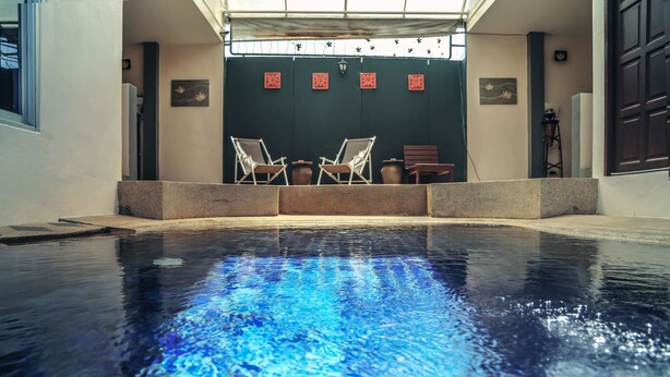 Uma piscina com duas espreguiçadeiras e uma mesa, cercada por um muro de pedra baixo.