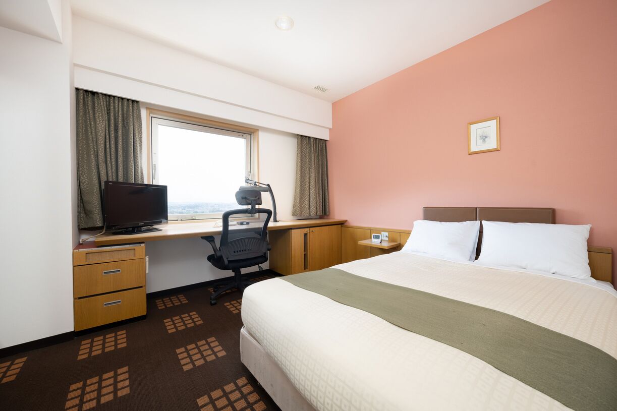 Ein Hotelzimmer mit Bett, Schreibtisch, Stuhl, Fernseher und Fenster.