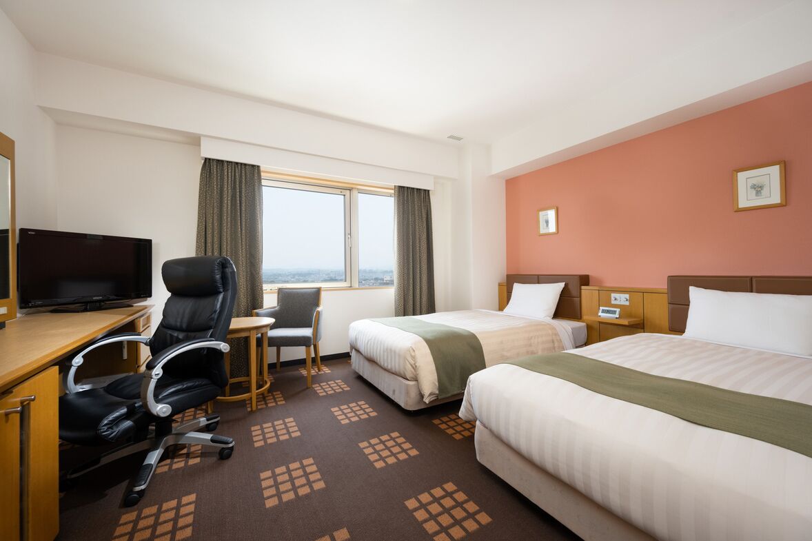 Ein Hotelzimmer mit Bett, Schreibtisch mit Stuhl, Fernseher und einem fensterbepflanzten Fenster.