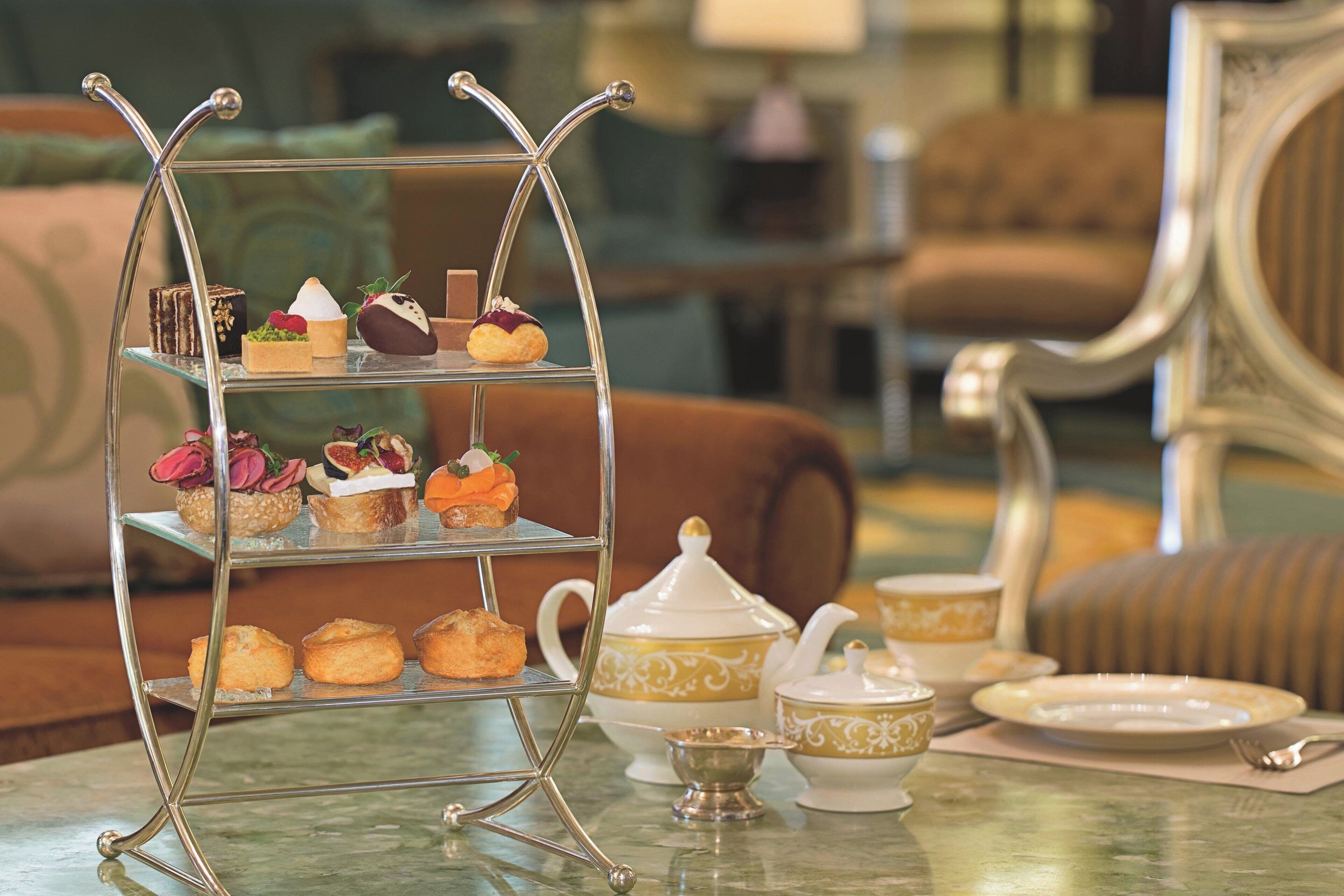 A three-tiered dessert stand with various pastries and a tea set on a table.