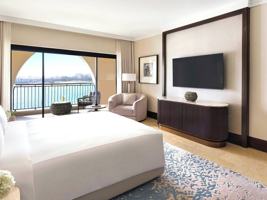Une chambre d’hôtel avec un grand lit, une télévision, une chaise, une petite table et une vue sur la ville par une grande fenêtre.