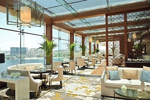 A spacious lounge area with high ceilings, large windows, and a view of a cityscape. - The Ritz-Carlton Abu Dhabi, Grand Canal (Abu Dhabi)