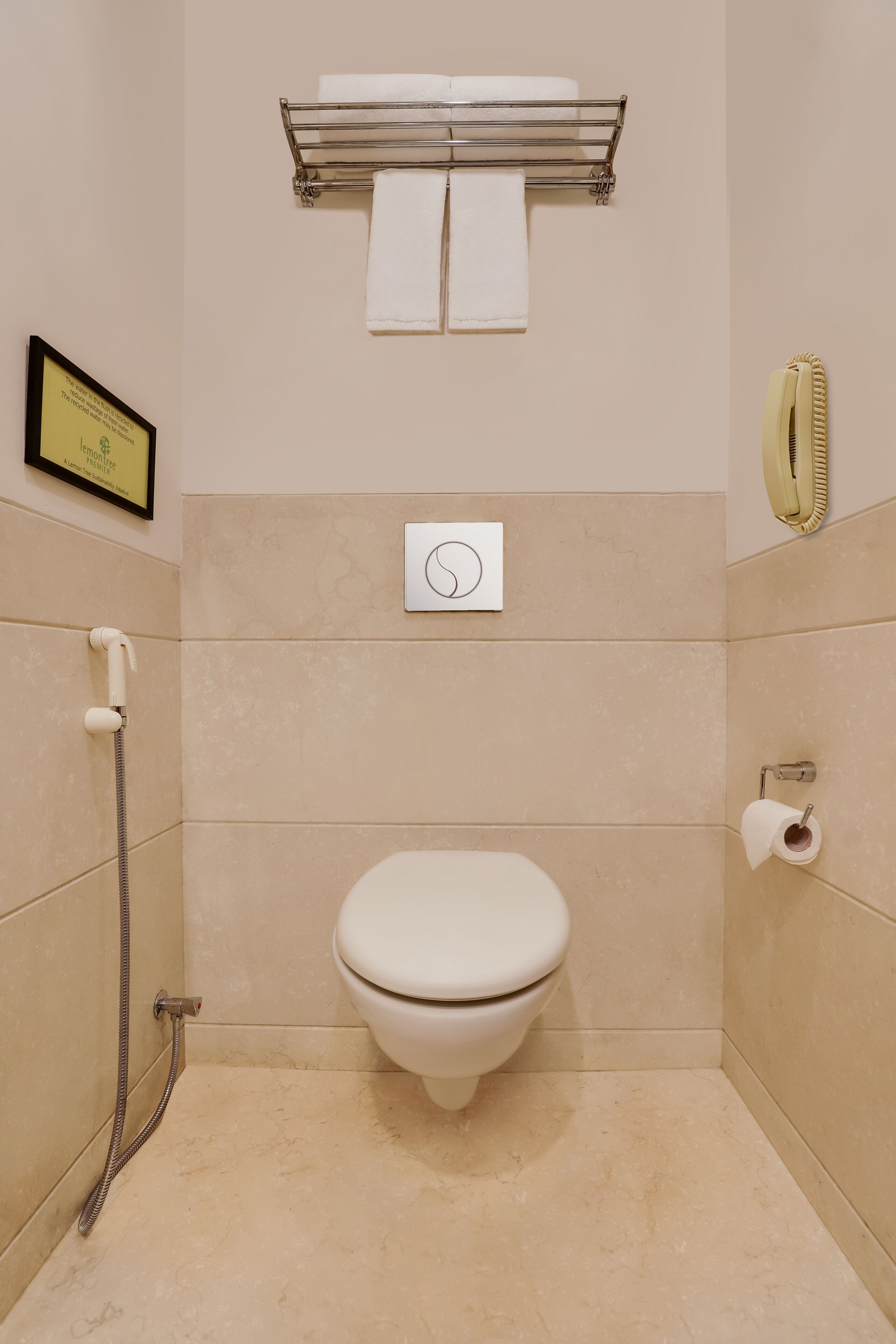 A bathroom with a toilet, a towel rack, a shower hose, and a framed certificate on the wall.