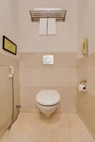 Een badkamer met een toilet, een handdoekhouder, een doucheslang en een ingelijst certificaat aan de muur.