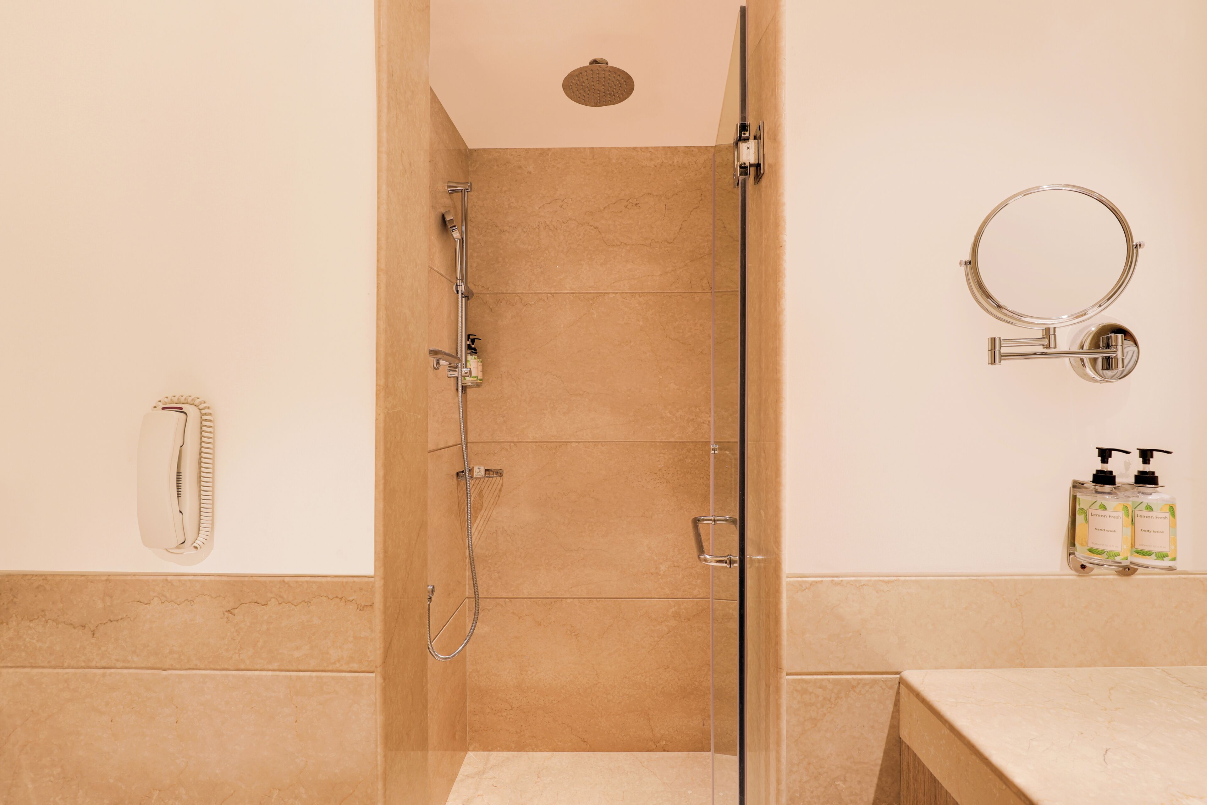 A bathroom with a glass shower enclosure, a handheld showerhead, a wall-mounted toilet paper holder, and a soap dispenser on the wall.
