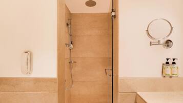 A bathroom with a glass shower enclosure, a handheld showerhead, a wall-mounted toilet paper holder, and a soap dispenser on the wall.
