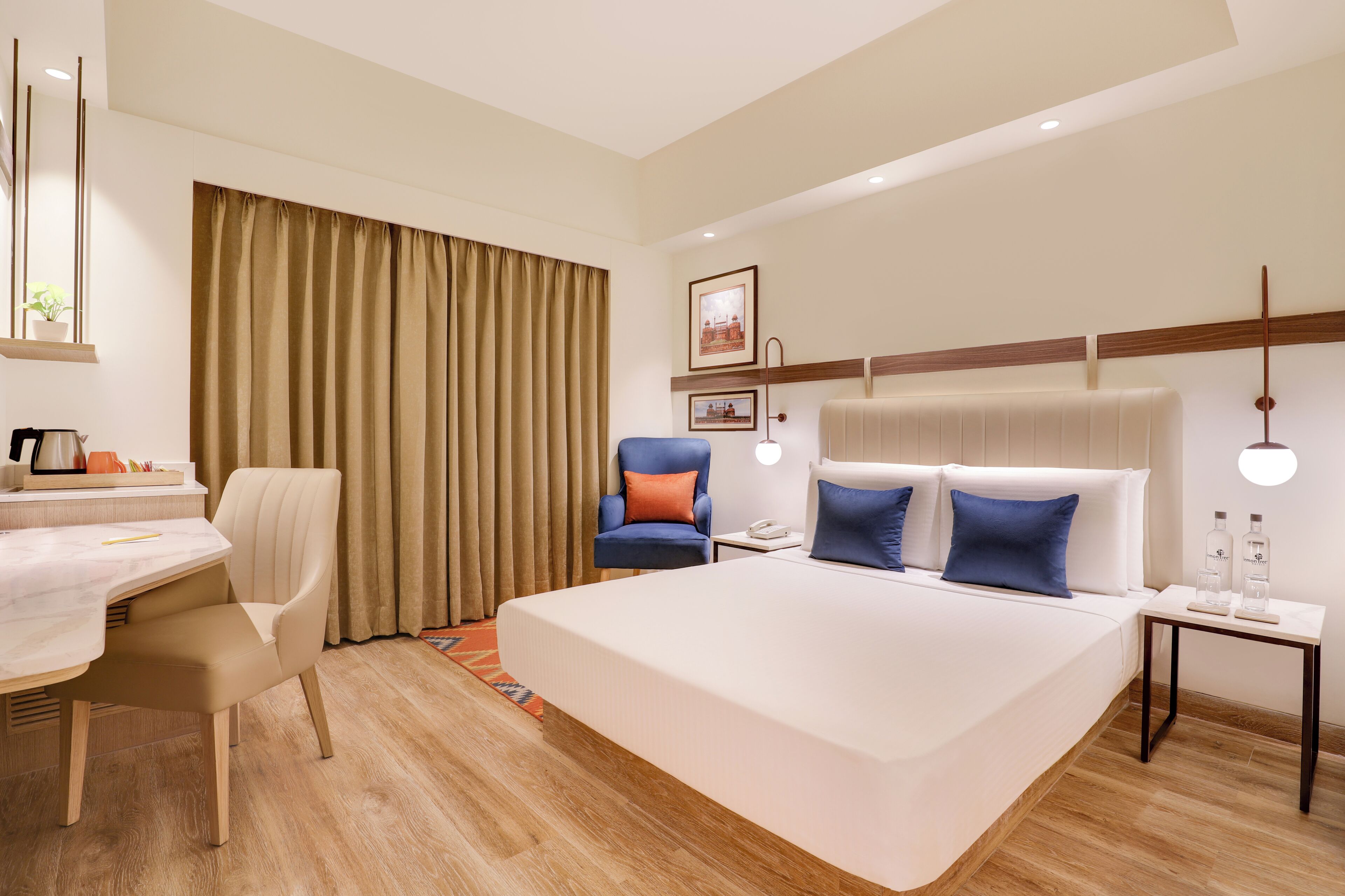 A hotel room with a large bed, a desk with a chair, a small table with a lamp, and a window with curtains.