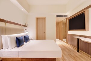 A modern hotel room with a bed, bedside table, and a flat-screen TV mounted on the wall.
