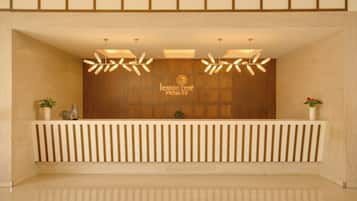 Un área de recepción con un panel de madera, una mesa de recepción con listones verticales e iluminación colgante.