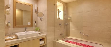 A modern bathroom with a large sink, a bathtub with rose petals, a mirror, and a shower.