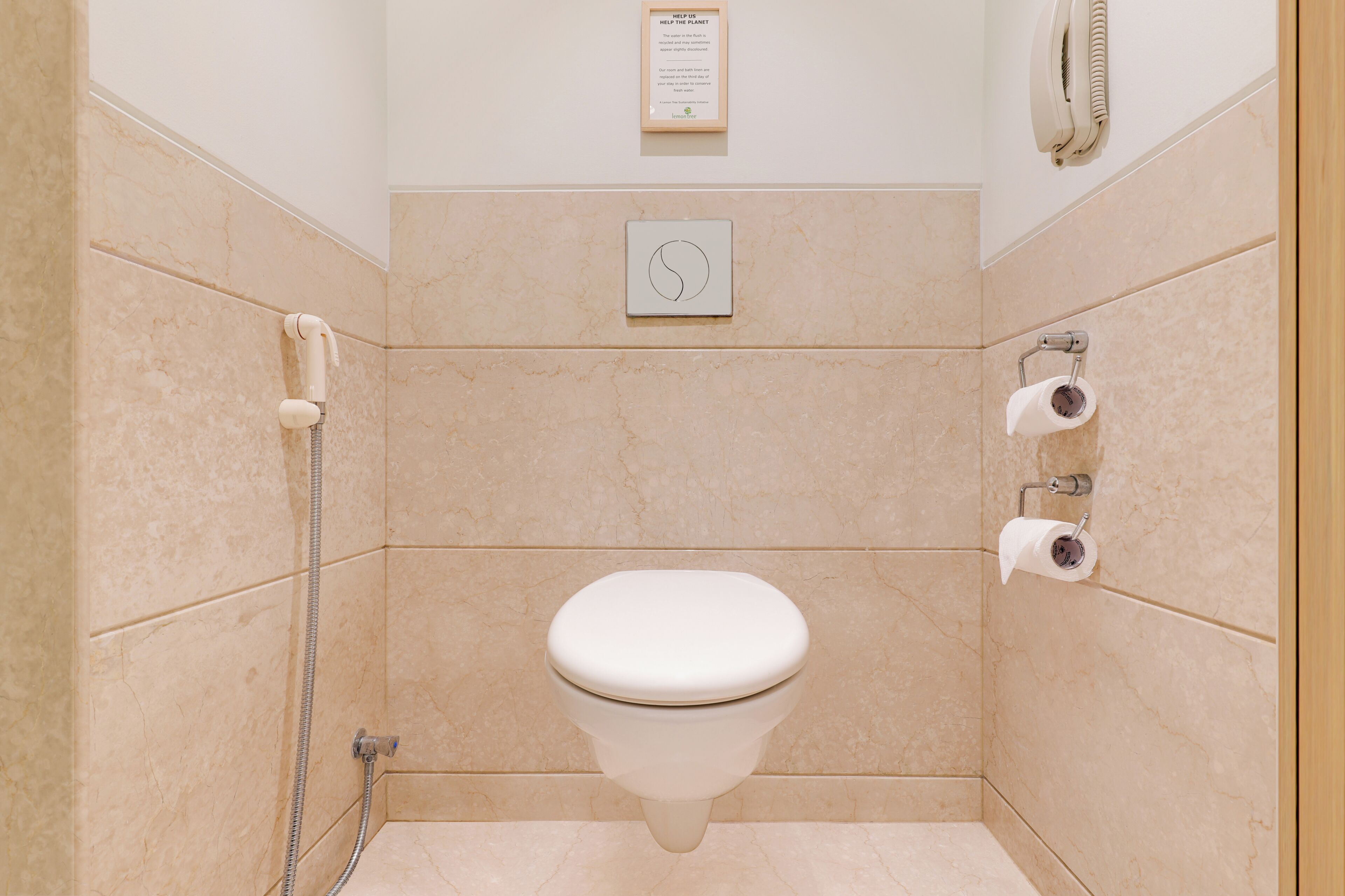 Un baño con inodoro, secamanos automático, dispensador de toallas de papel y porta rollos de papel higiénico en la pared.