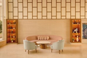 A modern interior with a curved sofa, two armchairs, a round coffee table, and built-in shelving with decorative items.