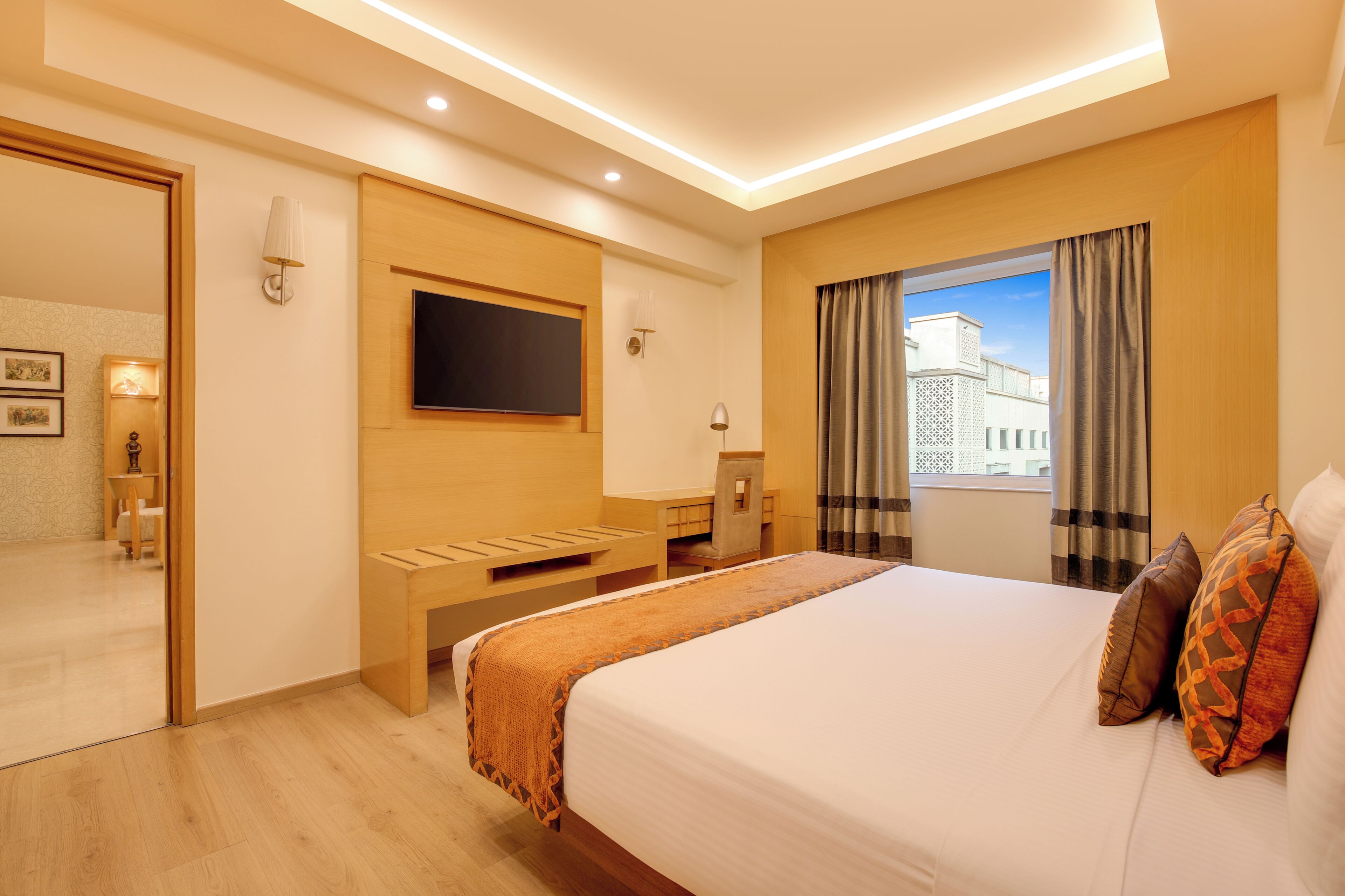 A hotel room with a bed, a desk, a chair, a TV, and a window with curtains.