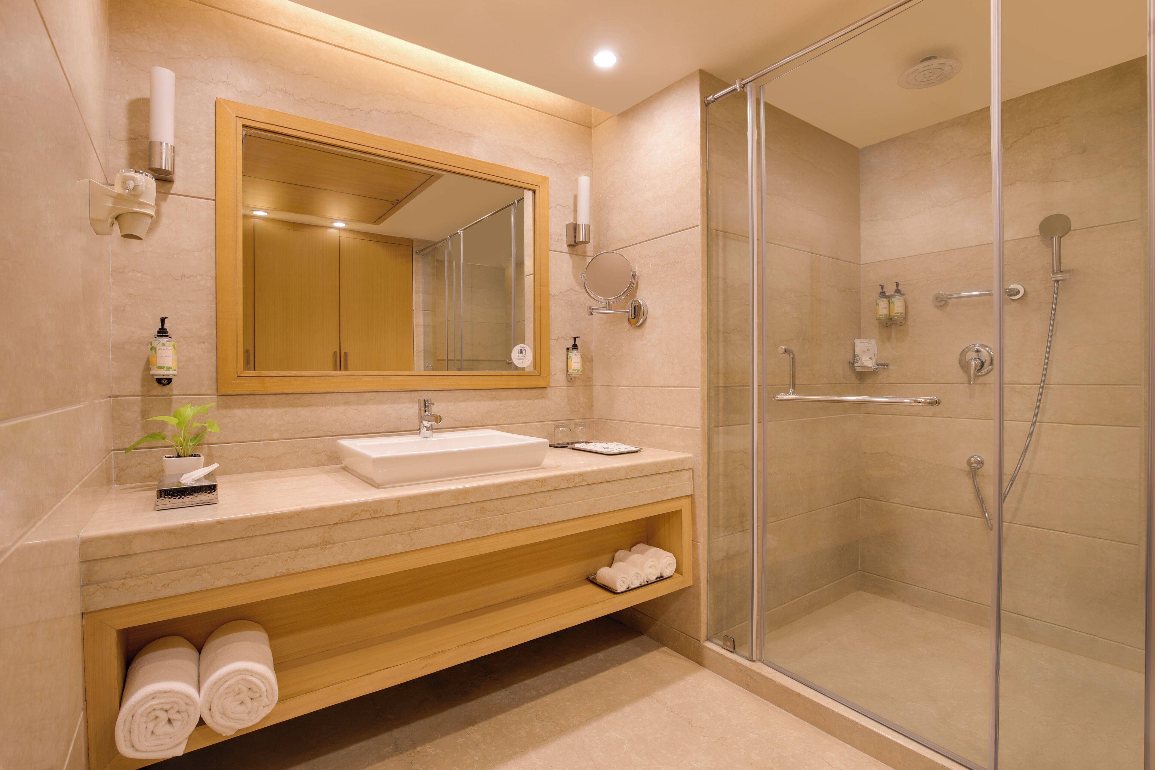 A modern bathroom with a sink, mirror, shower, and a shelf with towels.