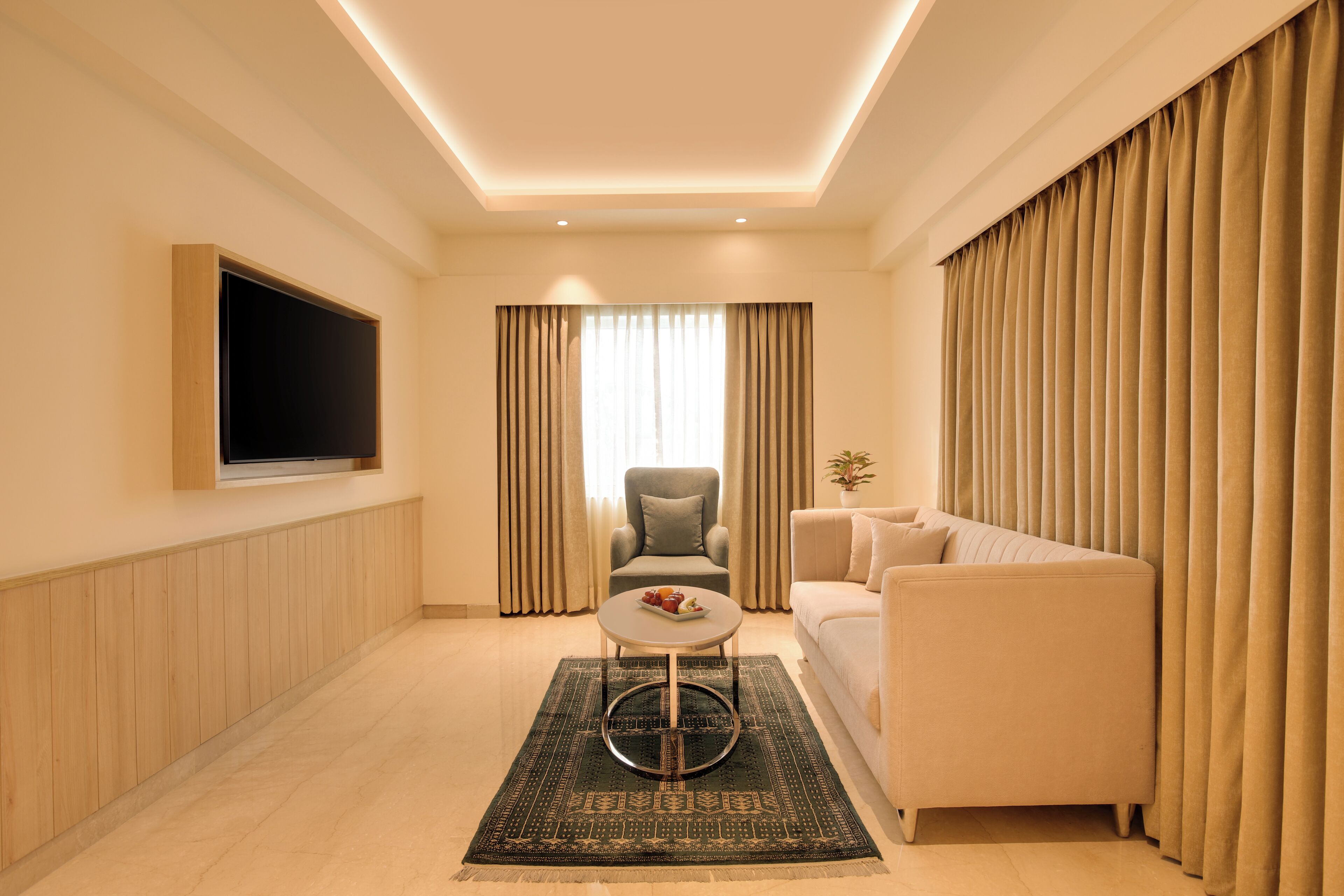 Una sala de estar moderna con una televisión de pantalla plana, un sofá, una silla, una mesa de centro y una alfombra estampada.