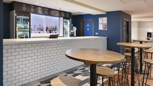 A bar area with a white tiled counter, a refrigerated display case, and multiple wooden tables and stools.