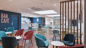 A modern bar café with teal and red chairs, wooden tables, and a blue accent wall.