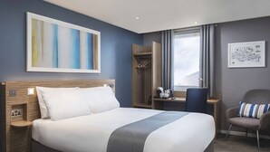 A modern hotel room with a large bed, a desk, a chair, and a window with a cityscape view. - Travelodge Liverpool Central Exchange Street (Liverpool)