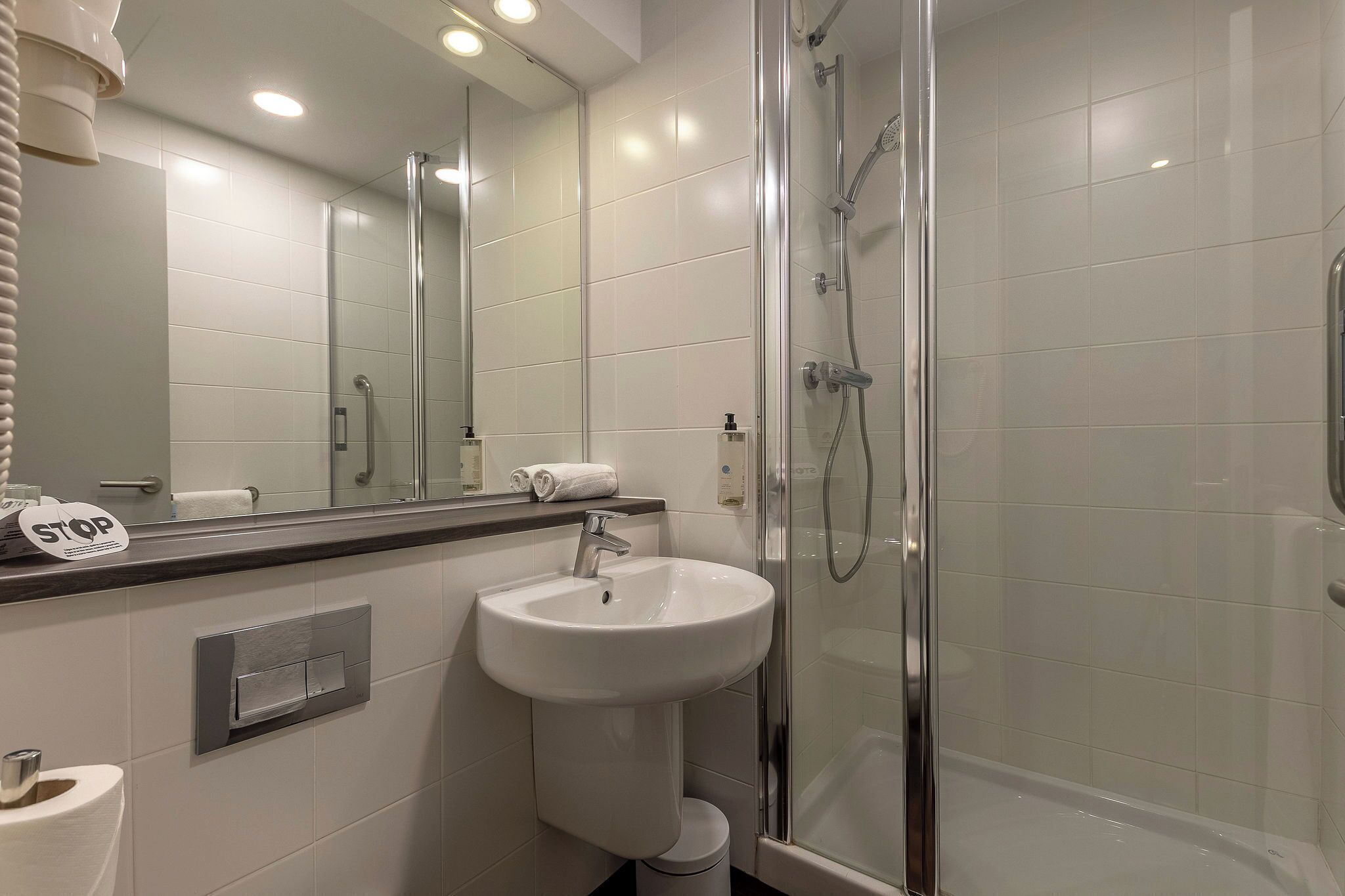 Un baño moderno con ducha de vidrio, un lavabo blanco y un espejo grande.