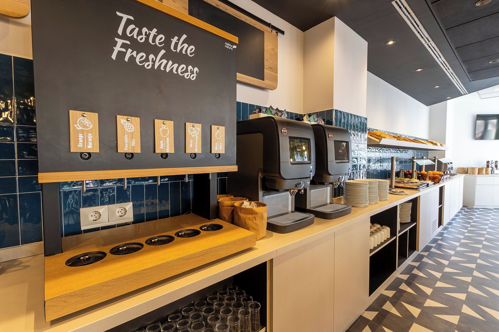 Ein modernes Café-Interieur mit einer Kreidetafel, auf der steht 'Frische genießen', einer Kaffeemaschine und einer Theke mit verschiedenen Kaffeekapseln.