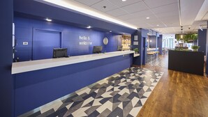Aula, jossa on sininen seinä, kello ja kyltti, jossa lukee: ”Tervetuloa!”.