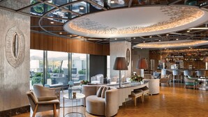 Een moderne hotel lobby met een centrale zithoek, grote ramen en een bar met diverse zitmogelijkheden.