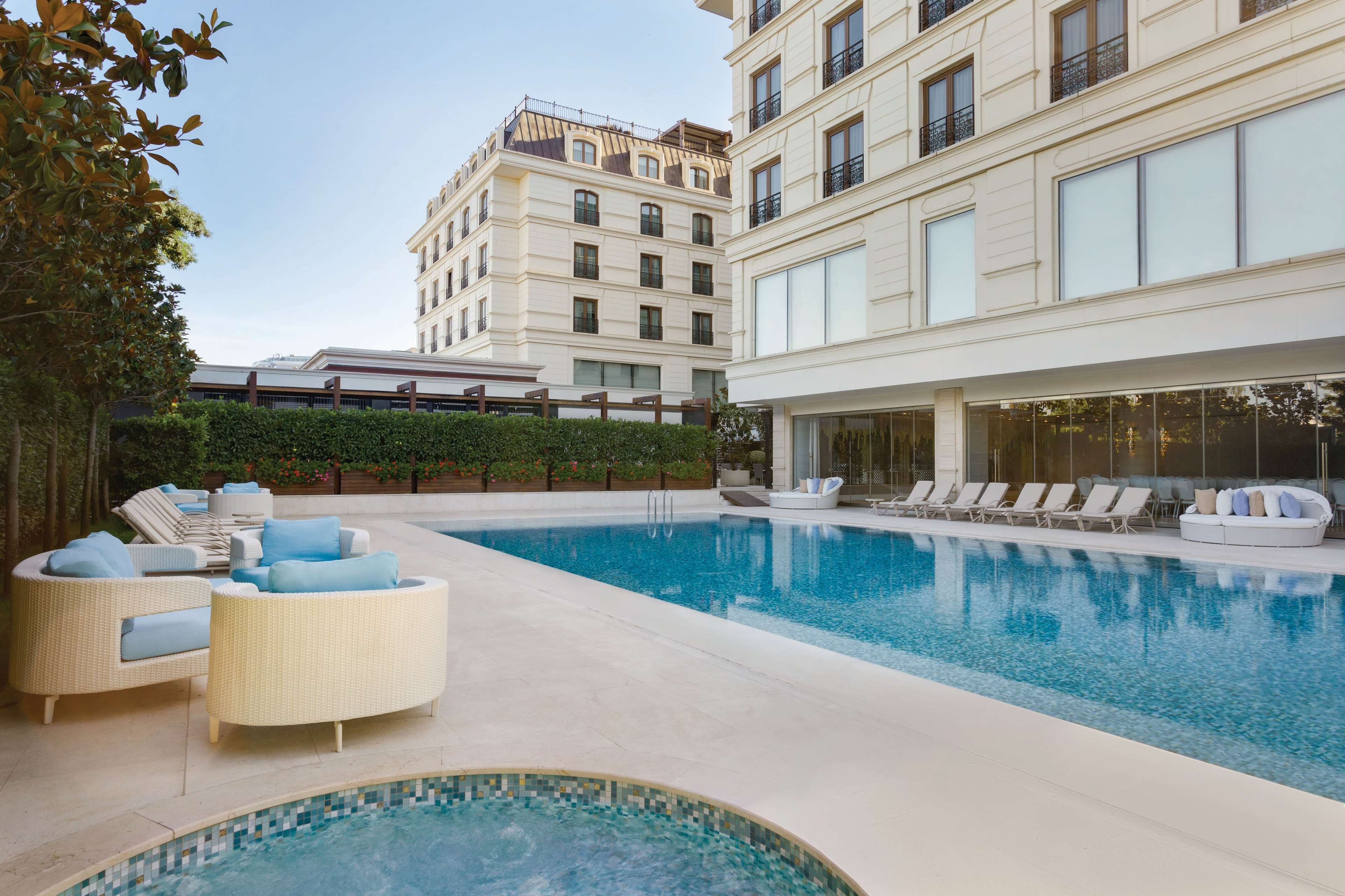 A swimming pool with lounge chairs and a hot tub, surrounded by a building with large windows and balconies.