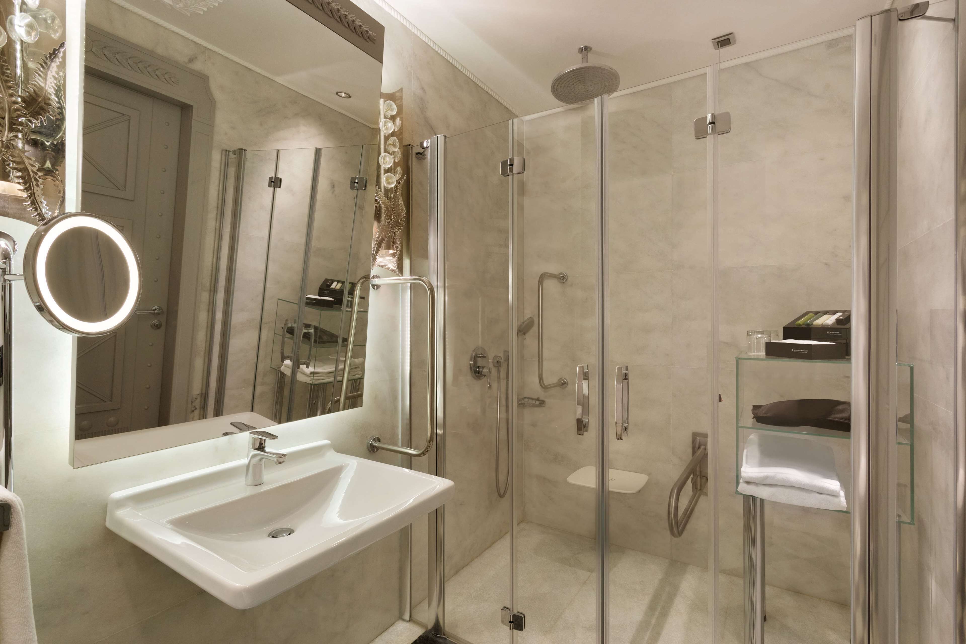 Une salle de bain moderne avec une douche à parois de verre, un lavabo avec un miroir et une étagère en verre où sont rangés les articles de toilette.