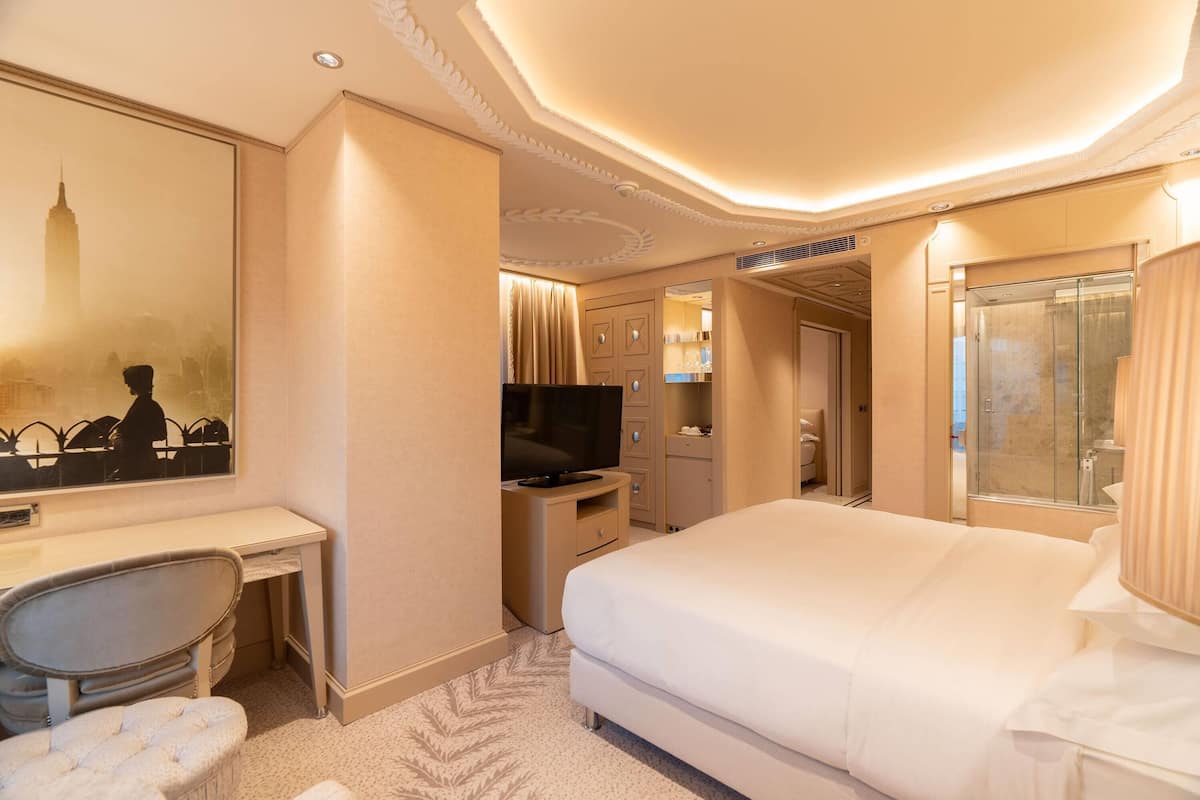 A hotel room with a bed, a desk, a television, and a bathroom with a glass shower.