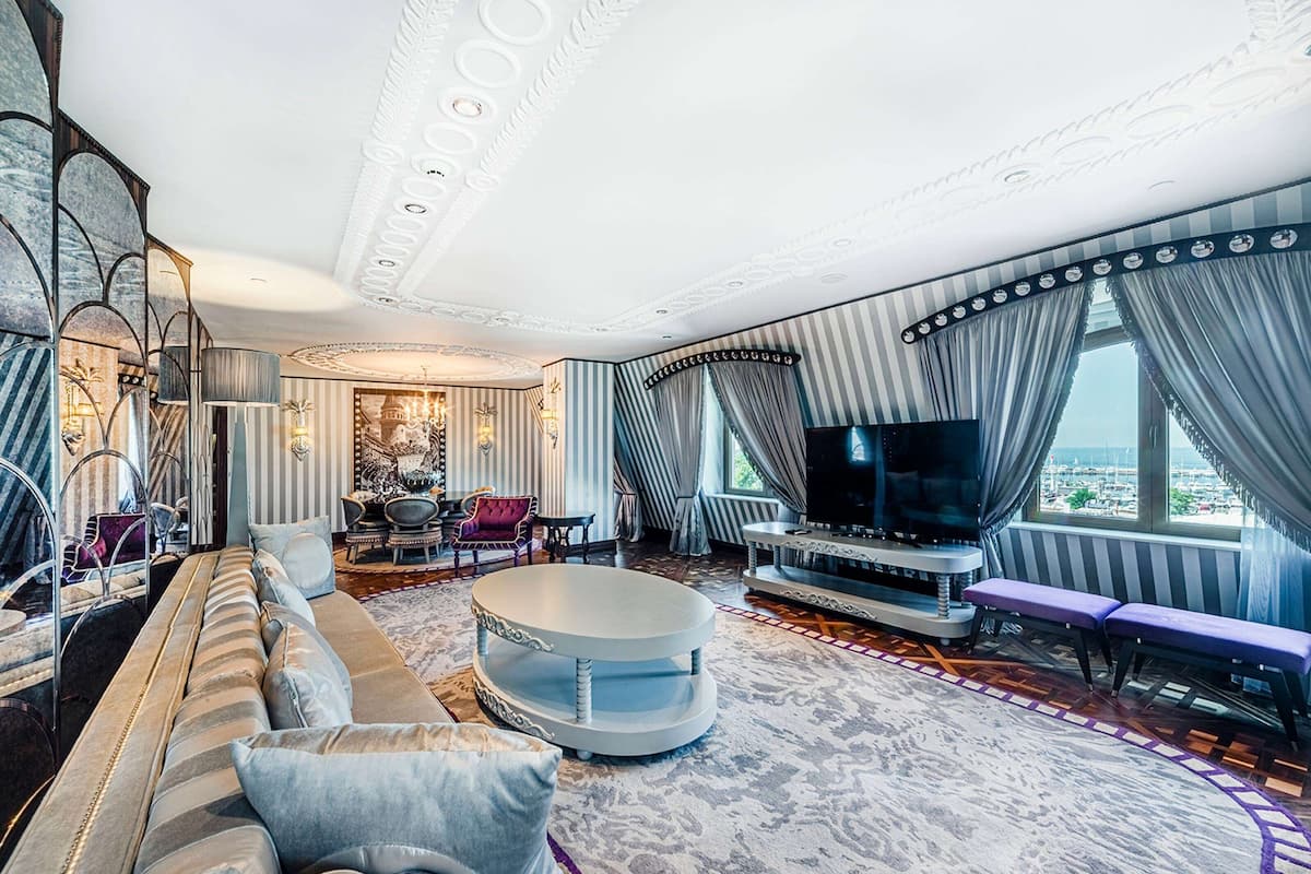 A luxurious living room with a large sofa, a round coffee table, a flat-screen TV, and a view of the city through large windows.