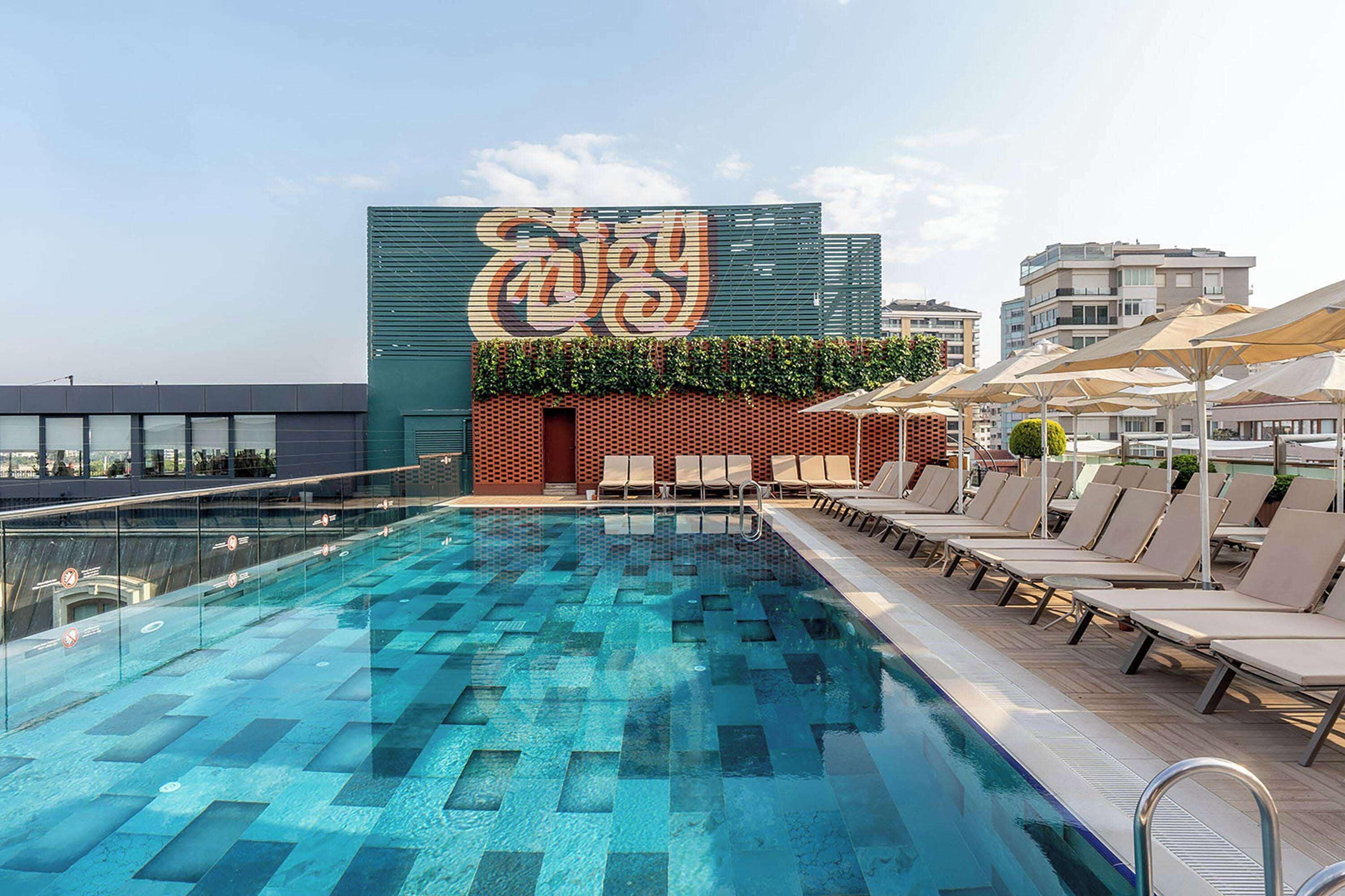 A rooftop pool with a geometric tile pattern, lounge chairs, and a large wall mural.