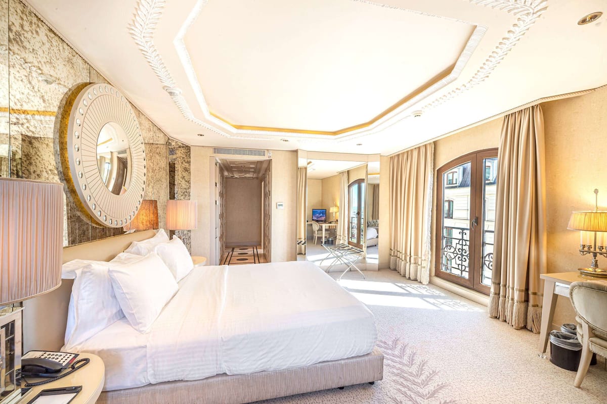 A spacious hotel room with a large bed, a desk, and a view through a glass door.