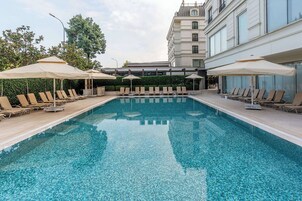A swimming pool with lounge chairs and umbrellas, surrounded by a building with large windows and a balcony.