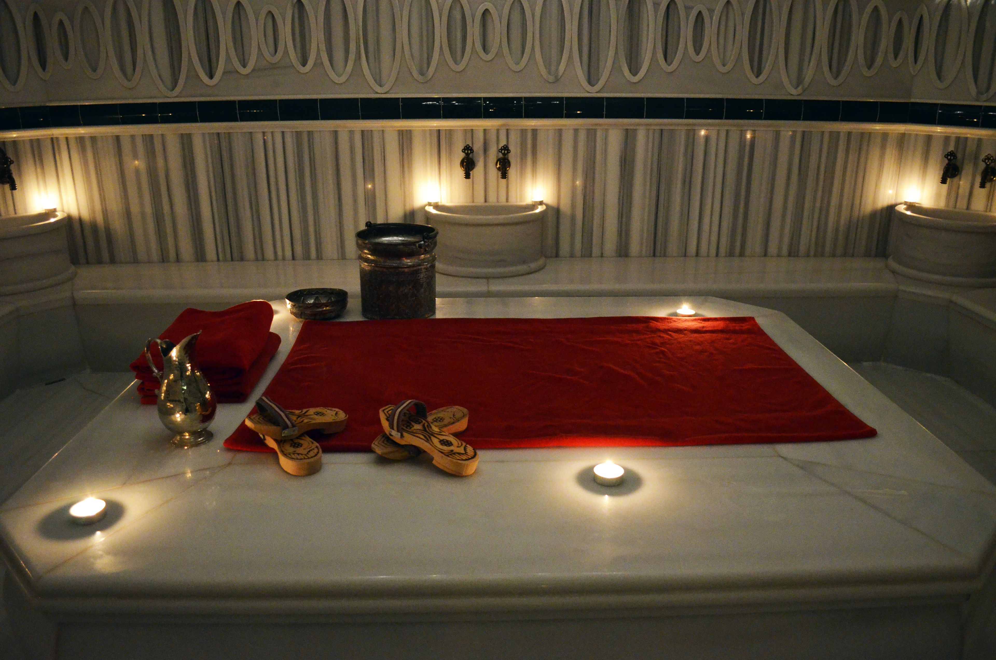 Ein Badezimmer mit einer Badewanne, einer roten Fußmatte, einem Paar Schuhe und einer Kerze.