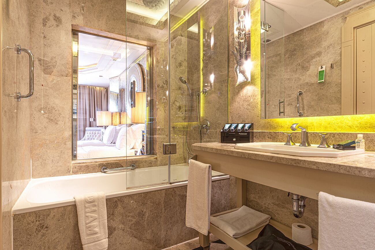 A modern bathroom with a bathtub, a large mirror, and a vanity with a yellow accent wall.