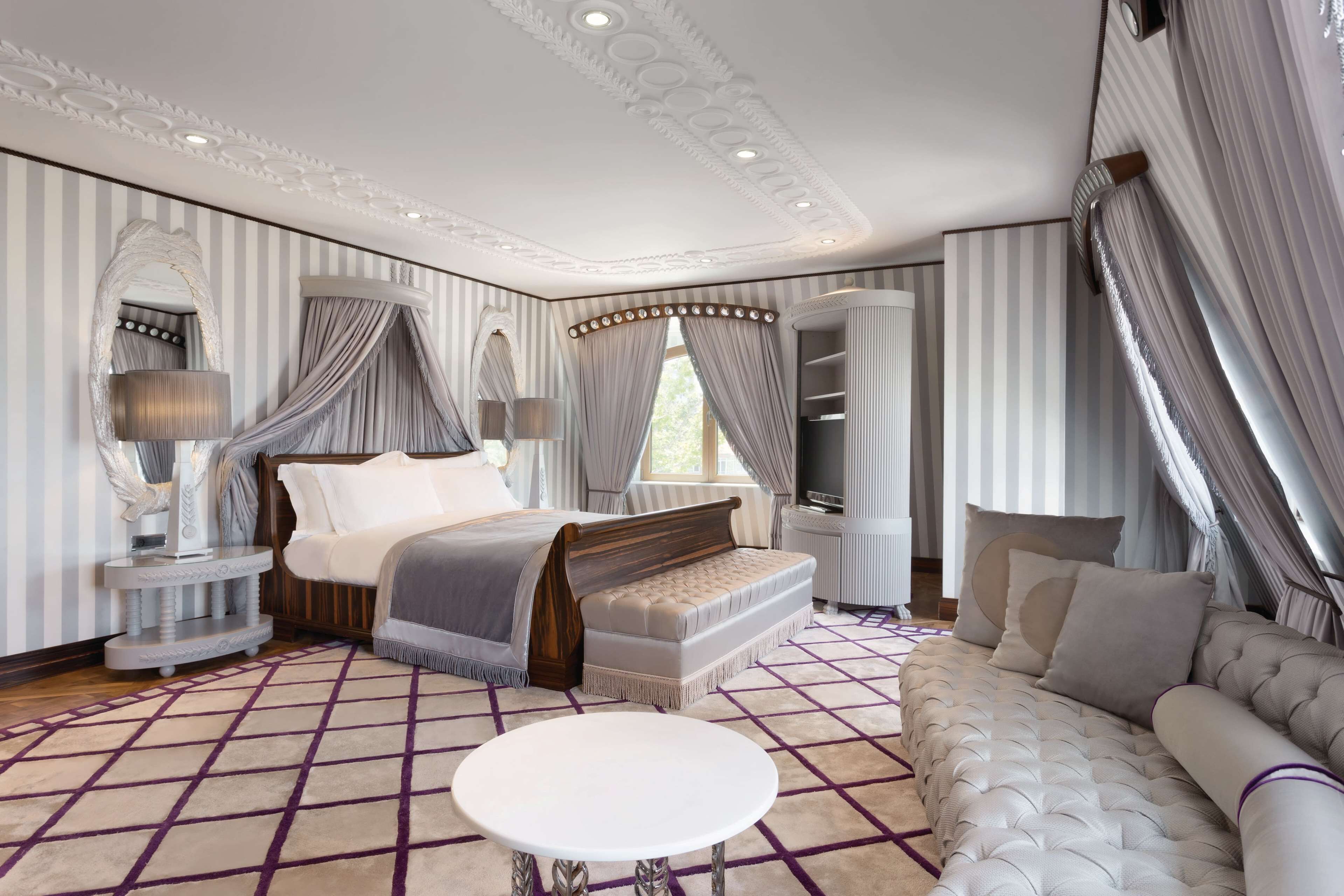 A bedroom with a large bed, a sofa, a round table, and a TV.