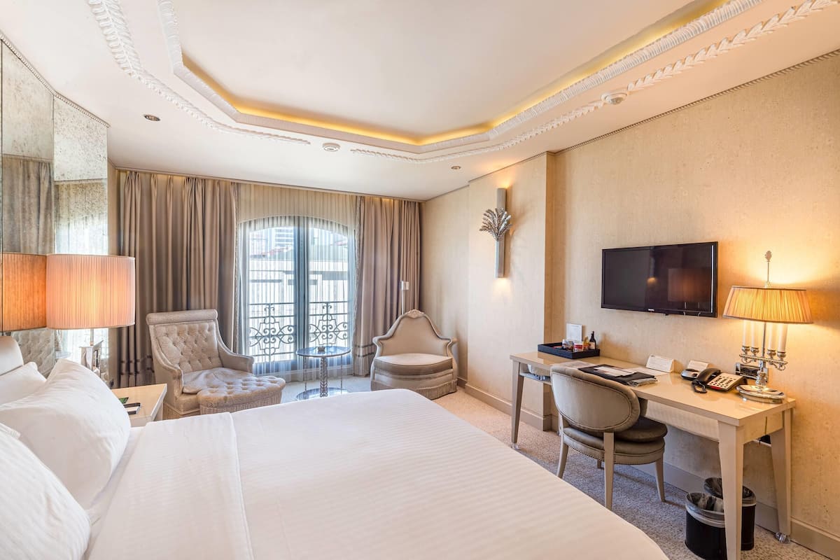 A hotel room with a large bed, a desk, a chair, a TV, and a window with curtains.