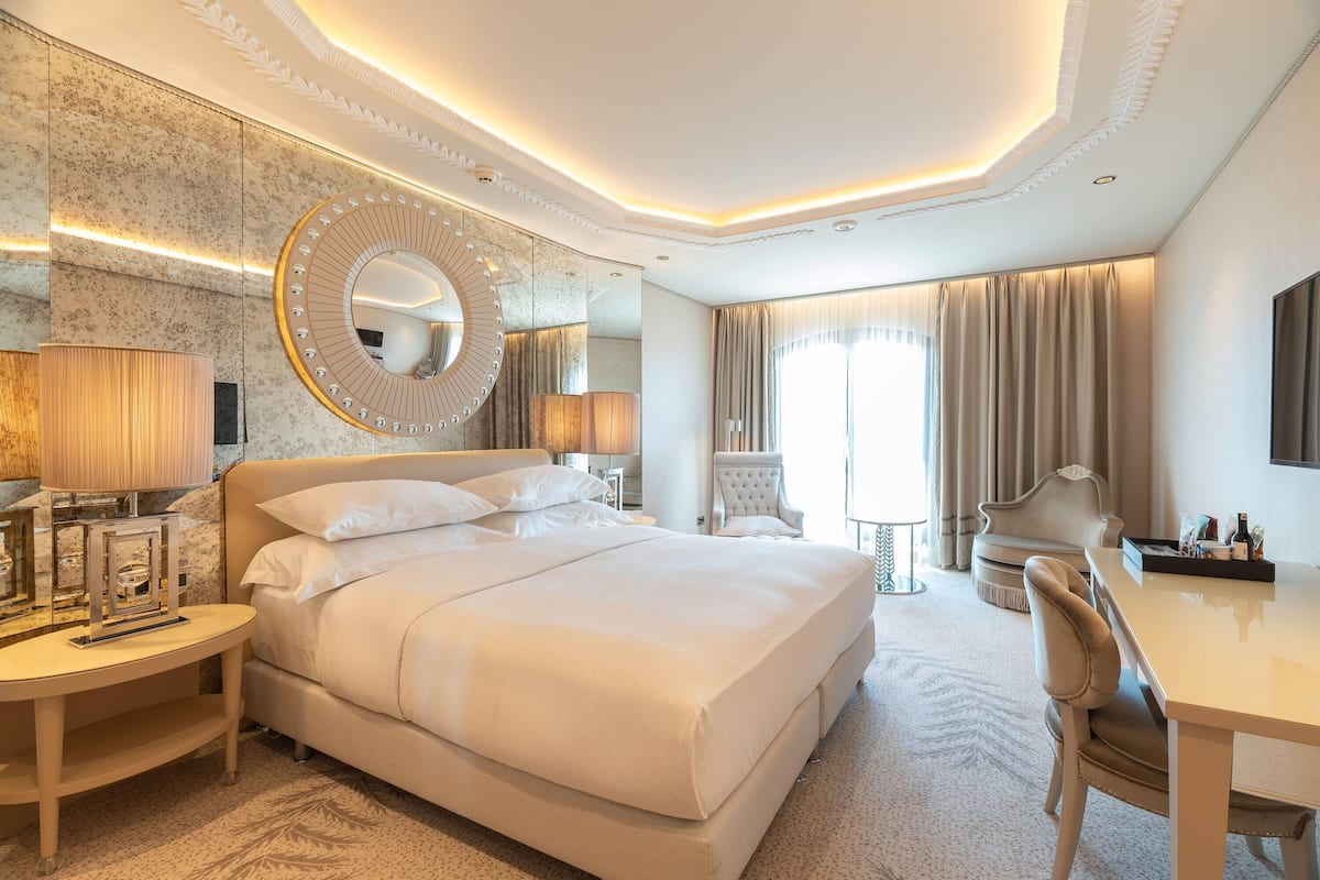 A hotel room with a large bed, a desk, a chair, a round mirror, and a television.