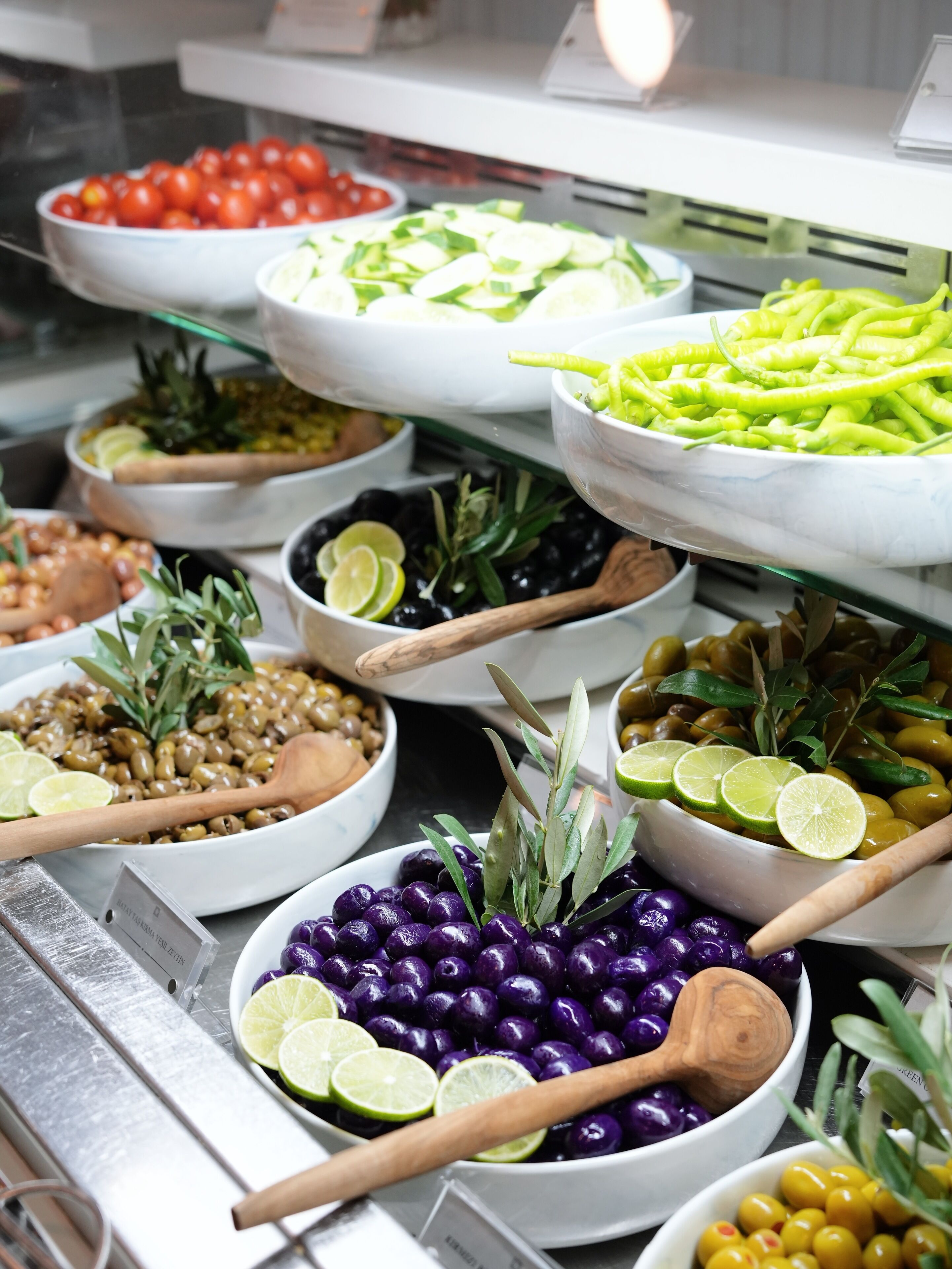A buffet with various food items including olives, tomatoes, cucumbers, and purple beans.