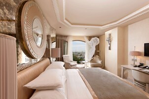 Una habitación de hotel espaciosa con una cama grande, un área de descanso con vistas, un espejo redondo y un escritorio con lámpara.