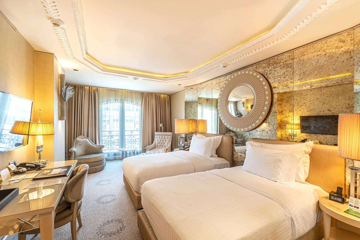 A hotel room with two beds, a desk, a chair, a TV, and a large mirror.