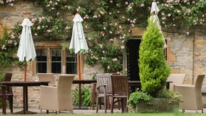 Un bâtiment en pierre doté d’un patio-jardin aménagé avec des meubles en osier et des parasols.